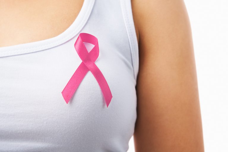 Mulher com camiseta branca e um laço rosa simbolizando o câncer de mama