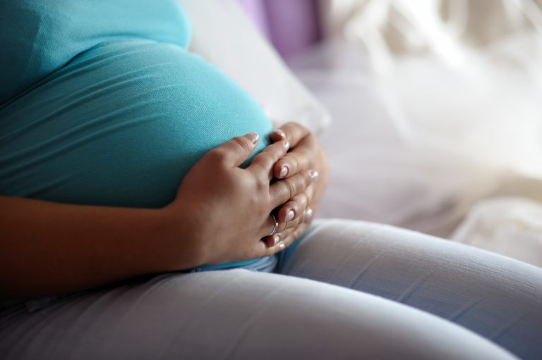 Mulher gestante está sentada segurando a barriga
