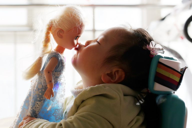 Uma menina está sentada beijando uma boneca