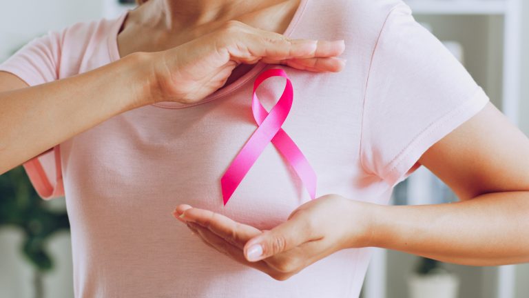 Uma mulher com uma camisa rosa e um laço rosa em cima da mama lembra a campanha de combate ao câncer de mama