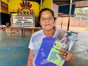 Anciã indígena da etnia guarani com cartazes da campanha de enfrentamento à violência contra a mulher.